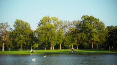 Suyun ortasındaki golf sahası, doğal manzara. Ağaçlı, yemyeşil bir manzaraya sahip arka plan. Yürüyen ya da rahatlatan insanlar. Yüksek kalite 4k görüntü