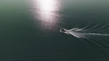 Mavi sularda ilerleyen bir sürat teknesinin havadan görüntüsü. Bir kişi teknenin arkasına çekiliyor, wakeboard ya da su kayağı yapıyor, dinamik bir duruşla suda oyuluyor. Yüksek kalite 4k görüntü