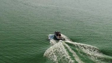 Dalgalı suda hareket eden bir sürat teknesinin havadan görüntüsü. Bir kişi teknenin arkasına çekiliyor, wakeboard ya da su kayağı yapıyor, dinamik bir duruşla suda oyuluyor. 4k görüntü