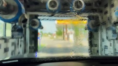 Otomatik oto yıkama sisteminden geçen bir arabanın içinden geniş çaplı görüntüler. Yıkandıktan sonra sıcak hava esiyor. Ön manzara. Yüksek kalite 4k görüntü