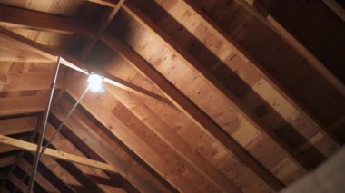 Açığa çıkmış ahşap çatı çerçevesi tek bir ampulle tamamlanmamış tavan arasını aydınlatıyor. Yüksek kalite 4k görüntü