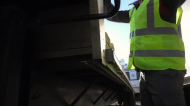 Genç Profesyonel Yarı Kamyon Şoförü, güneşli bir günde bir karavanı kamyona bağlayan bir güvenlik yeleği giyiyor. Ağır çekim. Yüksek kalite 4k görüntü
