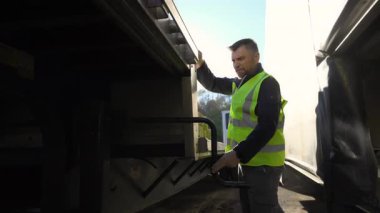 Genç, yakışıklı, yarı profesyonel kamyoncu güvenlik yeleği giyip güneşli bir günde karavanı kamyona bağlıyor. Ağır çekim. Yüksek kalite 4k görüntü