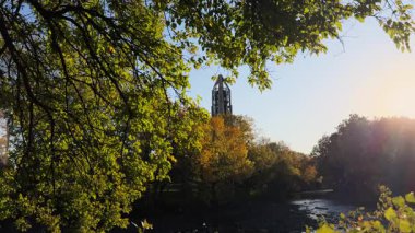 Güneşli bir yaz gününde yemyeşil ağaçların çerçevelediği Naperville Milenyum Carillon Kulesi manzarası. Sıcak güneş ışığı nehir kenarında barışçıl bir atmosfer yaratır. Yüksek kalite 4k görüntü