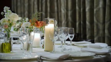 Restorandaki kutlama partisinde servis masasını bardaklar, tabaklar, çatal bıçaklar ve mumlarla kapatın. Düğün, doğum günü, kutlama partisi. Kamera ağır çekimde hareket ediyor. kalite 4k görüntü