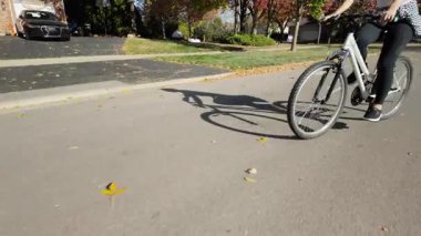 Caddede hızlı bisiklet süren bir kadının, güneşli havanın tadını çıkartan renkli yapraklarla çevrili görüntüsü. Yüksek kalite 4k görüntü