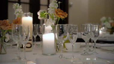 Restorandaki kutlama partisinde servis masasını bardaklar, tabaklar, çatal bıçaklar ve mumlarla kapatın. Düğün, doğum günü, kutlama partisi. Kamera ağır çekimde hareket ediyor. 4k görüntü