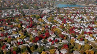 İnsansız hava aracı, kenar mahalle caddesini canlı kırmızı ve sarı sonbahar ağaçlarıyla çevrili olarak geniş açıdan görüyor. Sıcak sonbahar renkleri güzel mevsimsel mahalleler, evler yaratır. Yüksek kalite 4k görüntü