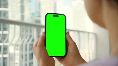 Balkonda Yeşil Ekranlı Akıllı Telefon Kullanan Kadın. Şehir Manzarası 'nda mobil uygulama modeli. Yüksek kalite 4k görüntü