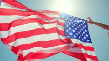 Arkaplanı açık mavi gökyüzü olan güçlü bir rüzgara karşı ABD bayrağını tutan kadın. Yüksek kalite 4k görüntü