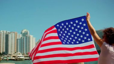 Miami 'nin arka planında güçlü bir rüzgara karşı ABD bayrağını tutan kadın. Yüksek kalite 4k görüntü