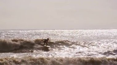 Genç sörfçü, Jacksonville, Florida 'da güneşli bir günde fırtınalı okyanus dalgalarında ustaca sörf yapar. Jacksonville FL 'de. ABD 2 Nisan 2025. Yüksek kalite 4k görüntü