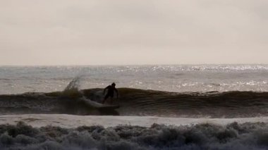 Genç sörfçünün silueti fırtınalı okyanus dalgalarında ustalıkla süzülüyor Jacksonville, Florida 'da güneşli bir günde. Jacksonville FL 'de. ABD 2 Nisan 2025. Yüksek kalite 4k görüntü