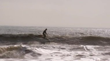 Sörfçü silueti, Florida 'da güneşli bir günde fırtınalı okyanusta ustaki dalgalarda ustalıkla yol alır. - Evet. Yüksek kalite 4k görüntü