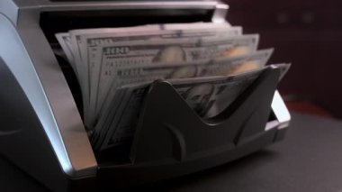 Para sayma makinesinin yan tarafı yakın çekim görüntüsü. Sayaç makinesi 100 dolarlık banknotları hesaplıyor. Ağır çekim. Yüksek kalite 4k görüntü