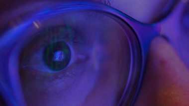 Kadın gözünün, ekranın yanıp sönen ışıklarını yansıtan gözlüklerden bakışını kapat. Yüksek kalite 4k görüntü