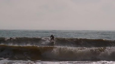 Genç sörfçünün silueti fırtınalı okyanus dalgalarında ustalıkla yol alan yaz güneşli bir günde Jacksonville, Florida 'da. Jacksonville FL 'de. ABD 2 Nisan 2025. Yüksek kalite 4k görüntü