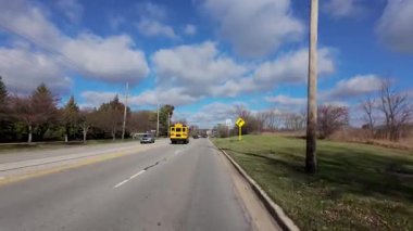 Okul otobüsünü banliyö caddesi boyunca takip eden araçtan POV görüntüsü. Sıcak sonbahar renkleri ve parlak mavi gökyüzü mahallelerin güzel bir resmini oluşturur. Yüksek kalite 4k görüntü