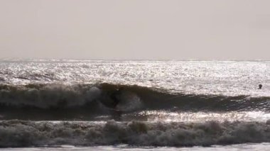 Florida, Jacksonville 'de güneşli bir yaz gününde fırtınalı okyanus dalgalarında ustalıkla sörf yapan genç sörfçünün silueti. Jacksonville FL 'de. ABD 2 Nisan 2025. Yüksek kalite 4k görüntü