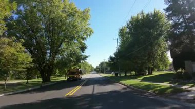 Hareket halindeki bir arabadan çekilen geniş bir görüntü okul otobüsü ve elektrik direklerinden, parlak ve güneşli bir sabahta ABD 'deki bir parkın yakınındaki yerleşim yerlerini yakalıyor. Yüksek kalite 4k görüntü