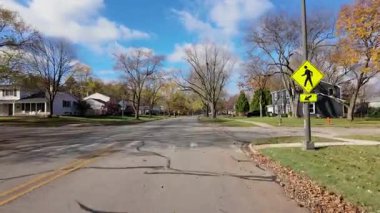 POV, sonbahar ağaçlarıyla dolu bir cadde boyunca hareket eden ve yaya geçidini işaret eden arabadan çekilmiş. Sıcak renkler ve bulutlu gökyüzü mahallelerin güzel bir resmini oluşturur. - Evet. Yüksek kalite 4k görüntü