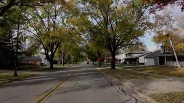 Pov, banliyö caddesi boyunca parlak sarı sonbahar ağaçlarıyla hareket eden arabadan çekilmiş. Sıcak sonbahar renkleri ve parlak mavi gökyüzü mahallelerin güzel bir resmini oluşturur. Yüksek kalite 4k görüntü