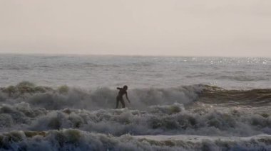 Florida, Jacksonville 'de güneşli bir günde fırtınalı okyanus dalgalarında ustalıkla sörf yapan genç sörfçünün silüeti. Jacksonville FL 'de. ABD 2 Nisan 2025. Yüksek kalite 4k görüntü