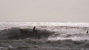 Florida, Jacksonville 'de güneşli bir yaz gününde fırtınalı okyanusun dalgalarında ustalıkla sörf yapan genç sörfçünün silueti. Jacksonville FL 'de. ABD 2 Nisan 2025. Yüksek kalite 4k görüntü