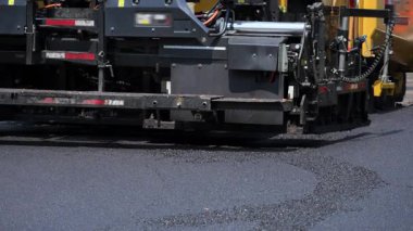 Asfalt asfalt asfalt makinesi yola yeni asfalt döşemiş. Bir yol inşaatı veya yeniden yüzeye çıkarma projesi kapsamında sıcak asfalt yüzeye eşit olarak yayılıyor. Yüksek kalite 4k görüntü