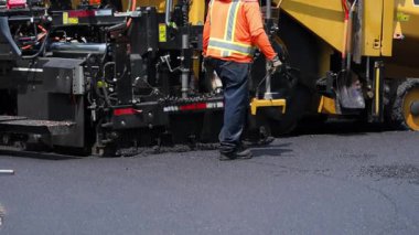 Asfalt asfalt asfalt makinesi yola yeni asfalt döşemiş. Yüksek görüş açısına sahip yelek giyen bir işçi kürek alıyor. Yüksek kalite 4k görüntü