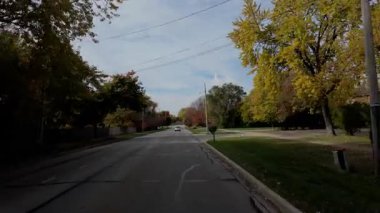 POV, parlayan sonbahar ağaçlarıyla birlikte yerleşim yeri caddesi boyunca hareket eden arabadan ateş ediyor. Sıcak renkler ve parlak mavi gökyüzü mahallelerin güzel bir resmini oluşturur. - Evet. Yüksek kalite 4k görüntü