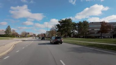 Dışarıdaki POV, güneşli bir günde küçük kasaba sokaklarında sonbahar ağaçlarıyla hareket eden arabadan ateş ediyor. Naperville lL 'de. 15 Mart 2025. Yüksek kalite 4k görüntü