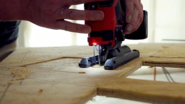 Yapboz elektrikli aletini kullanan kişi. İşçi iki eliyle yapboz tutuyor, tahta bir tahtanın üzerinde işaretli çizgiler boyunca ona rehberlik ediyor. - Evet. Yüksek kalite 4k görüntü