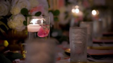 Restorandaki partide dekorasyon olarak sunulan servis masasını mumlar ve bardakta çiçekler ve suyla kaplayın. Düğün, doğum günü, kutlama partisi. Yüksek kalite 4k görüntü