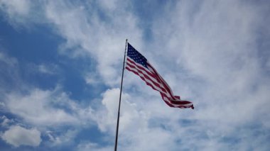 Bayrak direğinde dalgalanan ABD bayrağı, kabarık bulutlu, parlak mavi gökyüzünün arka planında. Yüksek kalite 4k görüntü