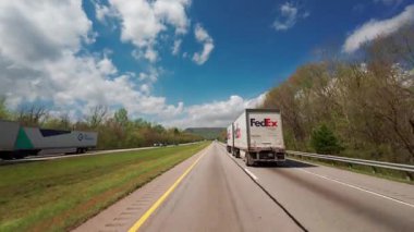 Çevresi yeşil bahar yapraklarıyla çevrili, dağınık bulutlu, parlak mavi bir gökyüzünün altında gezen FedEx dağıtım kamyonunun POV görüntüsü. Lojistik ve ulaşım konsepti. Atlanta GE. ABD 2 Mayıs 2025. Yüksek kalite 4k görüntü