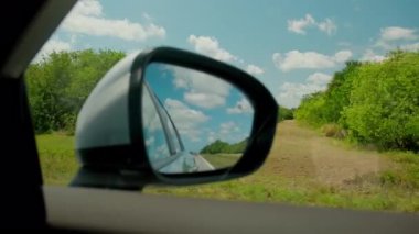 Güneşli bir günde yoldaki arabanın yan aynasında gökyüzü yansıması. Ön yolcu koltuğunun yan görüntüsü. Bulutlar aynada. Yüksek kalite 4k görüntü