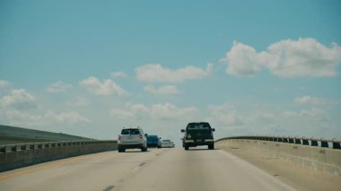 POV otobanda parlak mavi bir gökyüzünün altında kabarık bulutlar ve her iki tarafında yeşil bahar ağaçları ile ilerliyor. USA FL Miami 01 Nisan 2025. Yüksek kalite 4k görüntü