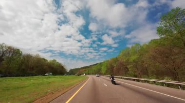 Otobanda motosiklet sürüşünün POV görüntüsü parlak mavi bir gökyüzünün altında kabarık beyaz bulutlar ve her iki tarafında yeşil bahar çiçekleri olan ormanlar. ABD TN Chattanooga 01 Nisan 2025. Yüksek kalite 4k görüntü