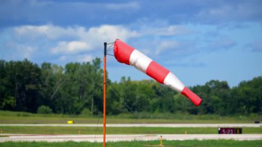 Red and white striped windsock mounted on a tall pole at an airfield. The windsock is extended, showing the wind direction and strength. High quality 4k footage