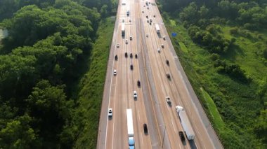 Highway road with the fast-moving vehicles, trucks showing U.S. transportation infrastructure under the bright sky in green suburbs. Drone view. High quality 4k footage
