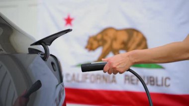 Close up of the electric car charging port. Plug in and disconnect of the charging port . California state flag background. High quality 4k footage
