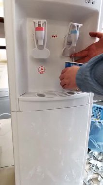 Su soğutucusundan bir bardağa su dolduran bir kadının elinin yakın çekimi. İçme suyunun faydaları kavramı. Dikey video.