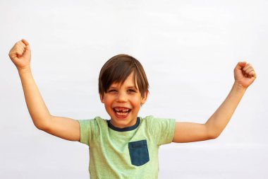 6 yaşında güzel bir Avrupalı çocuğun portresi, çocuk gülümseyip ellerini kaldırdı. Güzel ve mutlu bir çocuk. Yeşil tişörtlü beyaz bir arka planda izole edilmiş..