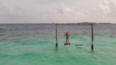 Maldivler Adası 'nın ve salıncaktaki kadının insansız hava aracı görüntüleri. Güzel okyanusun panoramik manzarası. Turizm ve tatil kavramı. Yüksek kalite 4k görüntü