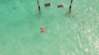 Maldivler Adası 'nın ve salıncaktaki kadının insansız hava aracı görüntüleri. Güzel okyanusun panoramik manzarası. Turizm ve tatil kavramı. Yüksek kalite 4k görüntü