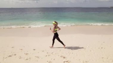 Kıyı şeridi boyunca koşan genç bir kadının hava takibi görüntüsü. Koşu aktivitesi sağlıklı yaşam tarzı olarak çok popülerdir.. 