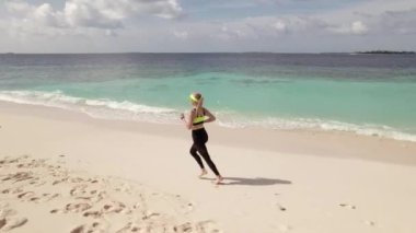Kıyı şeridi boyunca koşan genç bir kadının hava takibi görüntüsü. Koşu aktivitesi sağlıklı yaşam tarzı olarak çok popülerdir.. 