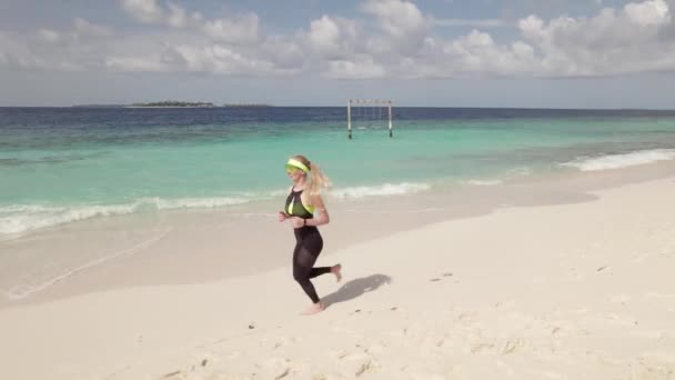 海岸線に沿ってジョギング若い女性の空中追跡ショット ランニング活動は健康的なライフスタイルとして非常に人気があります — ストック動画