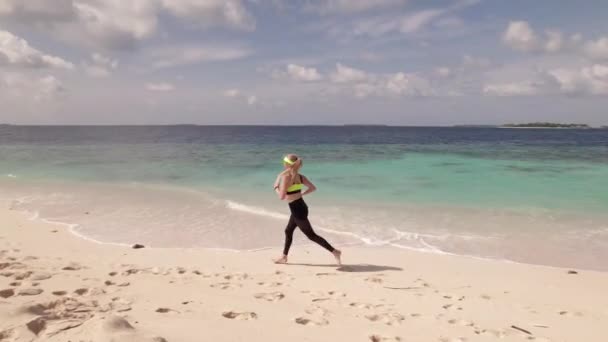 一个年轻女子沿着海岸线慢跑的空中跟踪镜头 跑步是一种很受欢迎的健康的生活方式 — 图库视频影像